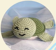 a crocheted green turtle laying on top of a white sheet with the eyes closed