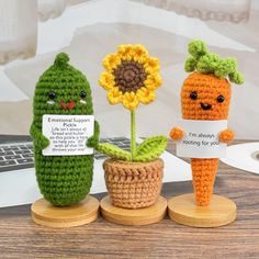 three crocheted carrots and a sunflower are sitting on small wooden stands