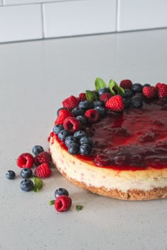 a cheesecake topped with berries and raspberries on a white counter next to blueberries