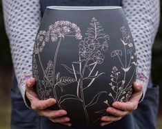 a person holding a vase with flowers painted on it