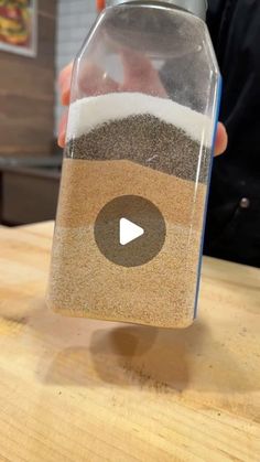 a person holding a jar with sand in it on top of a wooden countertop