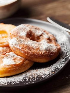 three powdered sugar donuts on a black plate