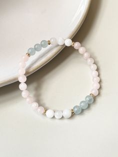 two bracelets with white and pink beads are on a table next to a plate