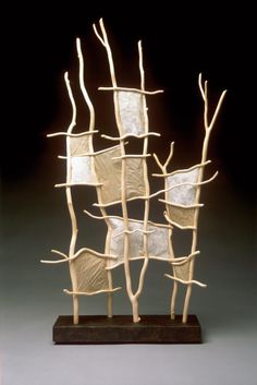 a sculpture made out of branches with white paper on it's sides and one piece of wood sticking out of the top