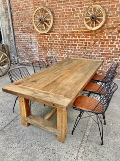 a wooden table sitting next to chairs on top of a cement floor in front of a brick wall