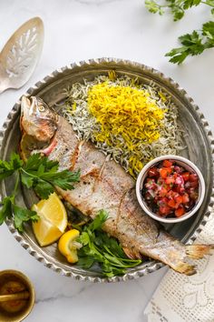 a fish and rice dish on a plate with lemons, cilantro, red peppers, and parsley