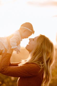 a woman holding a baby up to her face with the sun shining down on her