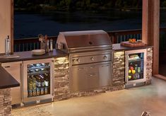 an outdoor kitchen with stainless steel appliances and stone counter tops, overlooking the water at night