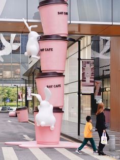 two people walking past a tall pink planter in the middle of a street with white rabbits on it