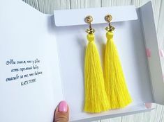 a pair of yellow tasselled earrings in a card with a hand holding it