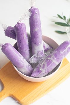 a bowl filled with purple candy sticks on top of a wooden cutting board