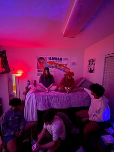 four people sitting on a bed in a room with pink lights and posters above them