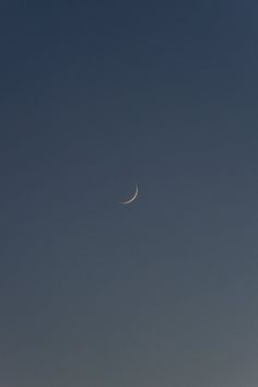 the moon is visible in the sky above some hills and trees on a clear day