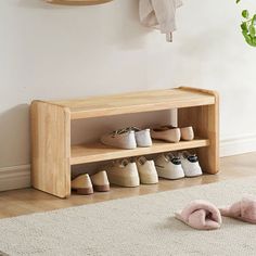 a wooden shoe rack with several pairs of shoes on it next to a rug and potted plant