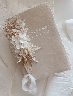 a wedding album with white flowers and ribbon tied around the cover is laying on a bed sheet