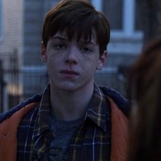 a young man with freckles on his face standing in front of a building