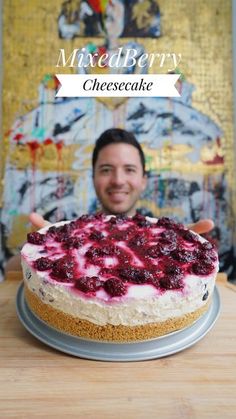 a man is holding up a cheesecake with berries on it and the words mixed berry cheesecake in front of him