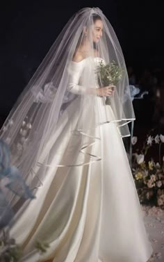 a woman in a wedding dress and veil walking down the aisle with flowers on it