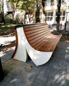 a curved wooden bench sitting on top of a brick walkway next to a tree filled park