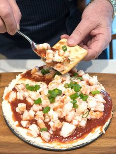 a person is spooning some food out of a small pizza on a plate with the words layered shrimp cocktail spread over it