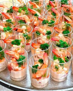 many small cups filled with shrimp and garnishes on a silver platter