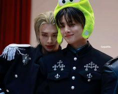 two young men in black uniforms with green hats on their heads and one wearing a yellow frog hat