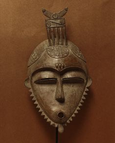 a decorative mask hanging on the wall in front of a brown background with an ornate headdress