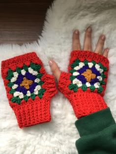 a woman's hand wearing red knitted mittens with colorful flowers on them