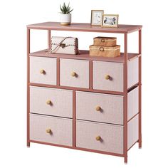 a pink dresser with drawers and pictures on the top, next to a potted plant