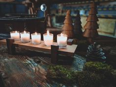 several lit candles sit on a wooden table in front of pine cones and fir trees