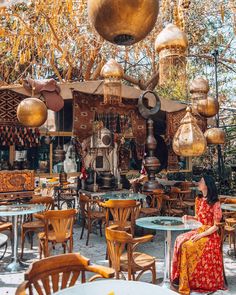 a woman sitting at an outdoor cafe with lots of tables and chairs in front of her