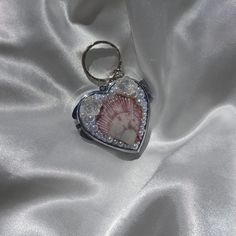 a heart shaped keychain with a seashell in the center on a white satin background