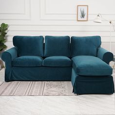 a blue couch sitting on top of a white floor next to a rug and potted plant