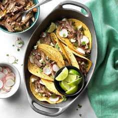 three tacos in a pan with limes and cilantro on the side