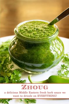 a jar filled with green pesto next to some parsley on a white plate