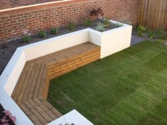 a wooden bench sitting on top of a lush green field next to a brick wall