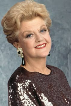 an older woman with blonde hair wearing a sequined top and smiling at the camera