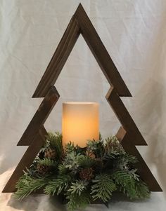 a candle is lit in front of a wooden triangle with pine cones and greenery