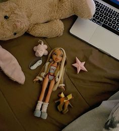 a laptop computer sitting on top of a bed next to a doll and other toys