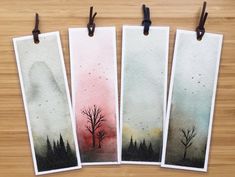 three watercolor paintings hanging from clothes pins on a wooden table next to each other