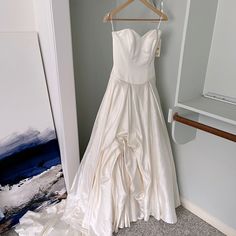 a wedding dress hanging on a hanger next to a wall with a painting in the background