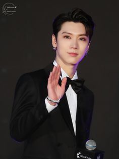 the young man is wearing a tuxedo and holding his hand up in front of him