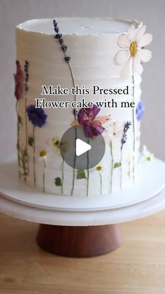 a white cake with flowers on it sitting on top of a wooden table next to a sign that says make this pressed flower cake with me