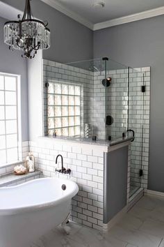 a white bath tub sitting under a chandelier next to a window in a bathroom