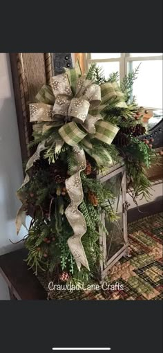 a christmas arrangement with pine cones, evergreens and bows on a table in front of a window