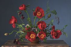 a vase filled with red flowers sitting on top of a wooden table next to a blue wall