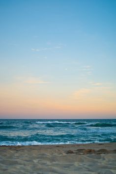 an empty beach with waves coming in to shore and the sun setting on the horizon