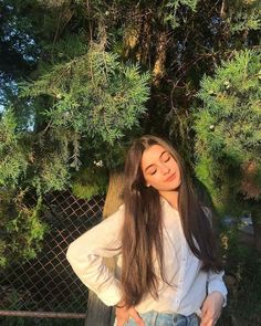 a girl standing in front of a tree with her hands on her hips and looking at the camera