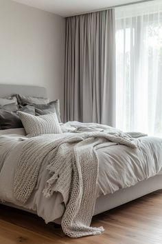 a bedroom with a large bed covered in grey sheets and blankets next to a window