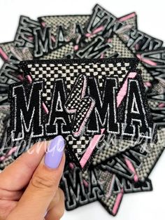 a hand holding up a patch with the word mamma on it in pink and black